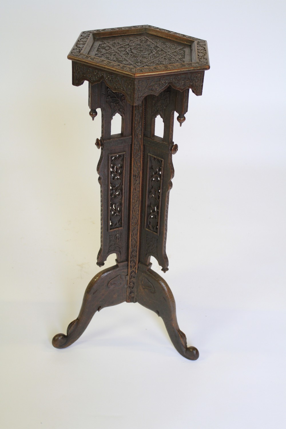 A dark brown carved wood hexagonal lamp table featuring pierced floral panels, a tray top, and curved tripod feet.