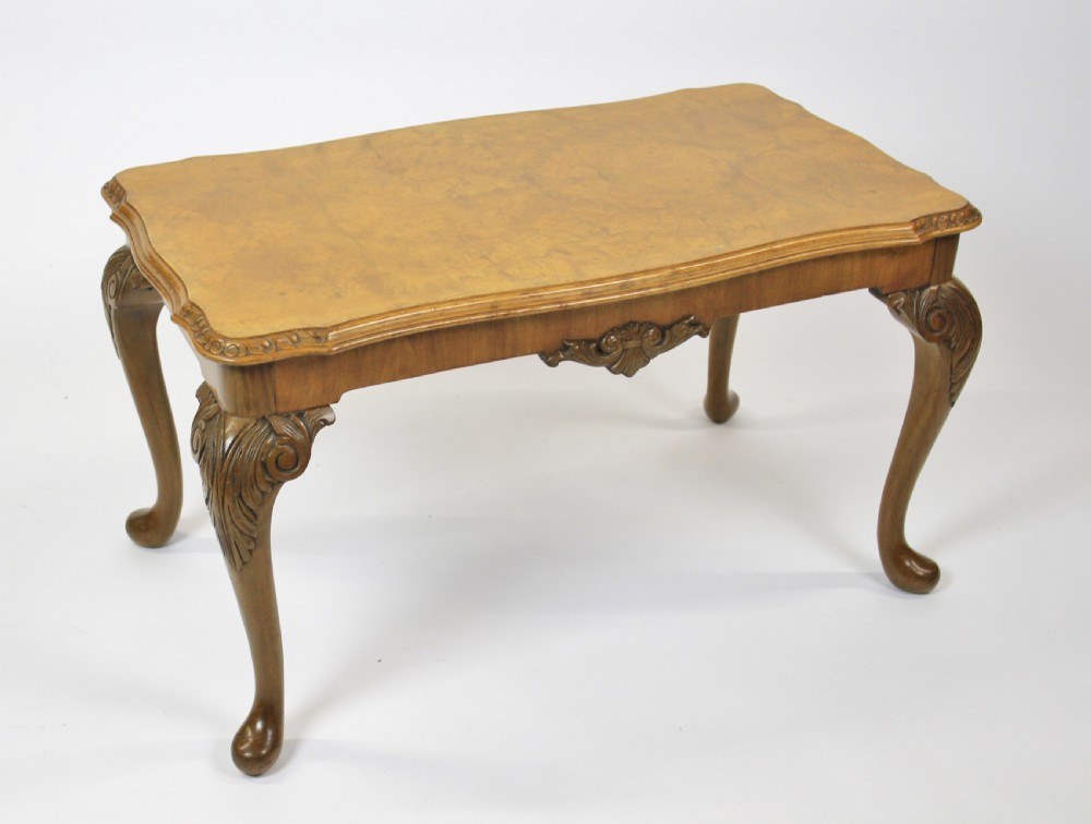 A low rectangular burr walnut coffee table featuring a serpentine edge, carved central shell motif, and four carved cabriole legs.