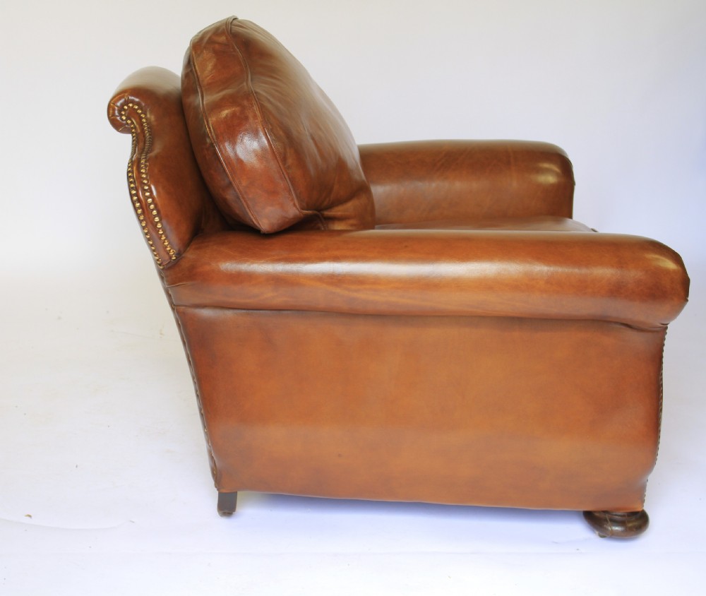 A pair of 1920s tan leather club armchairs featuring rolled arms, brass stud trimming, shaped crest backs, and turned wooden feet on castors. View III