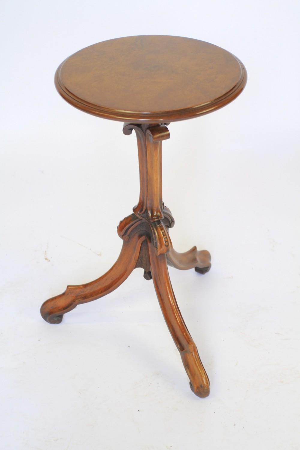 A Victorian circular burr walnut lamp table resting on a carved central column and tripod legs.