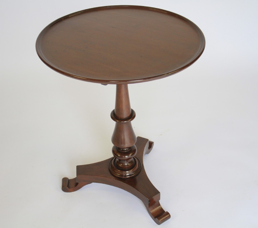 A William IV dark mahogany tilt-top table featuring a raised moulded edge rim, a turned central pedestal stem, and a tri-form platform base on scroll feet. View II