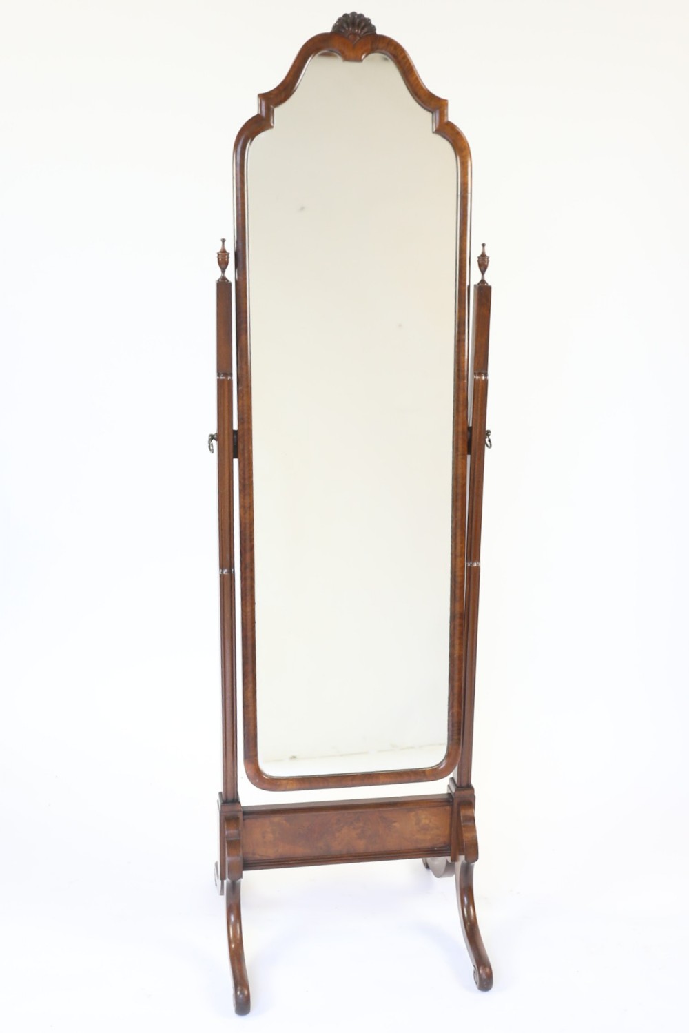 A full-length walnut cheval mirror featuring an arched frame with a carved shell motif crest, turned side support posts, and splayed legs.
