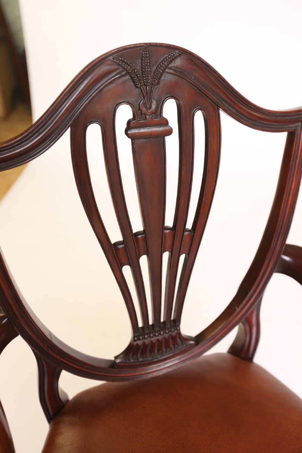 A pair of 1930s Hepplewhite style mahogany elbow chairs featuring carved shield backs and tan leather seats. View IV