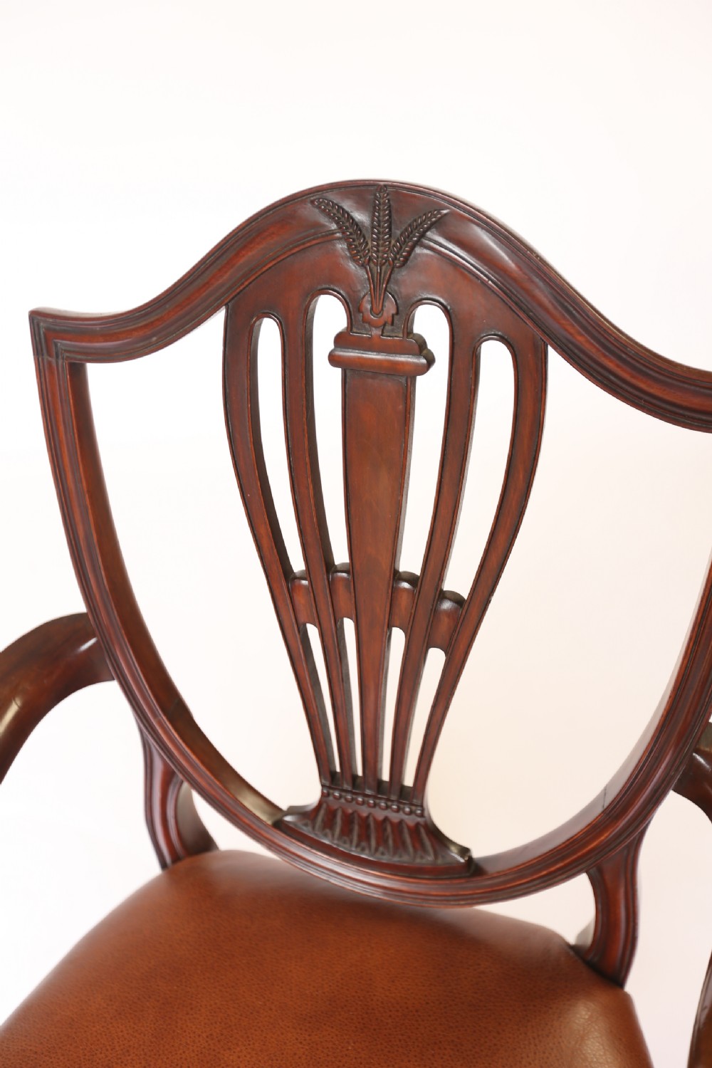 A pair of 1930s Hepplewhite style mahogany elbow chairs featuring carved shield backs and tan leather seats. View VII