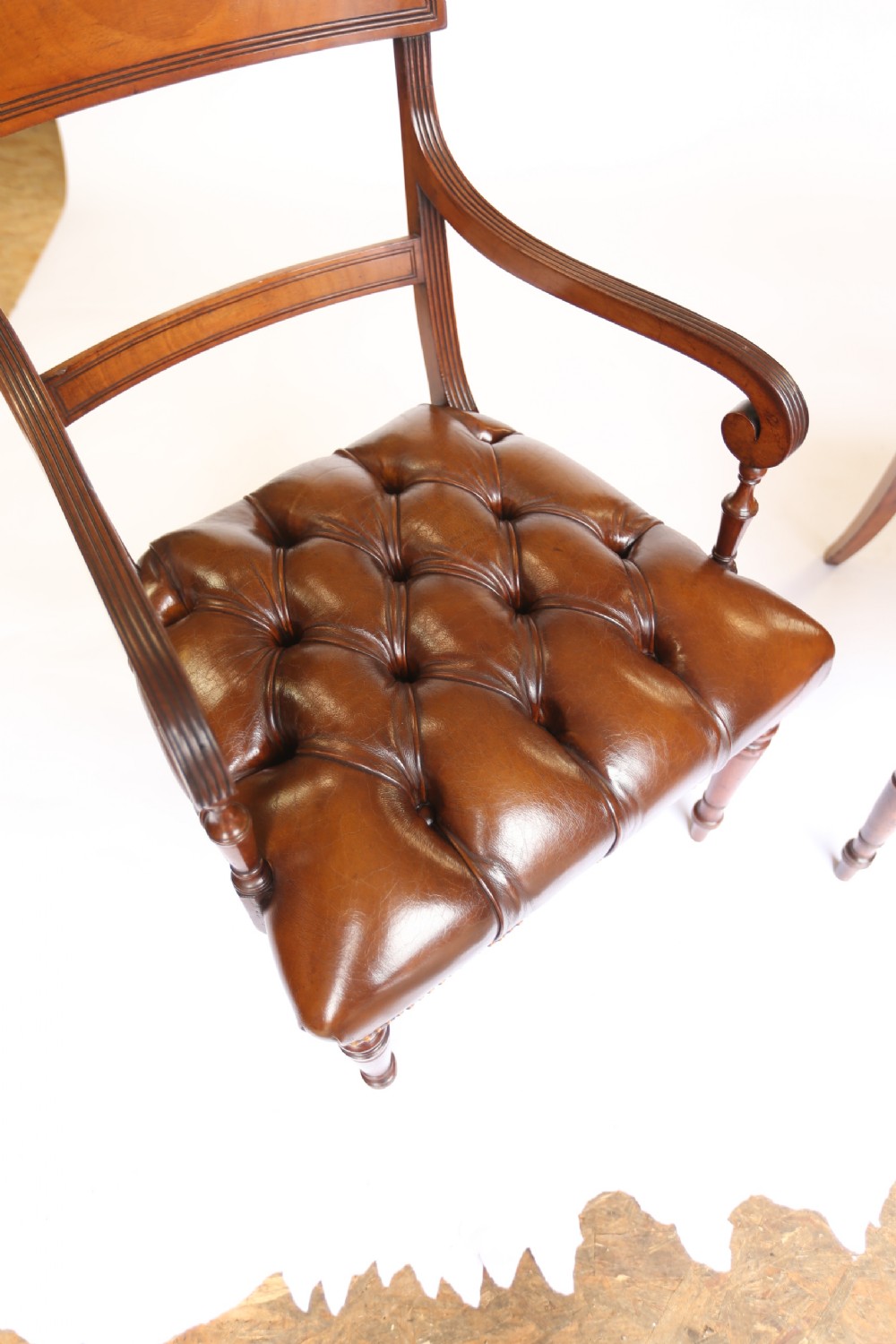 A pair of 19th-century mahogany elbow chairs featuring reeded arms, button-tufted brown leather seats with brass studding, and turned front legs. View VI