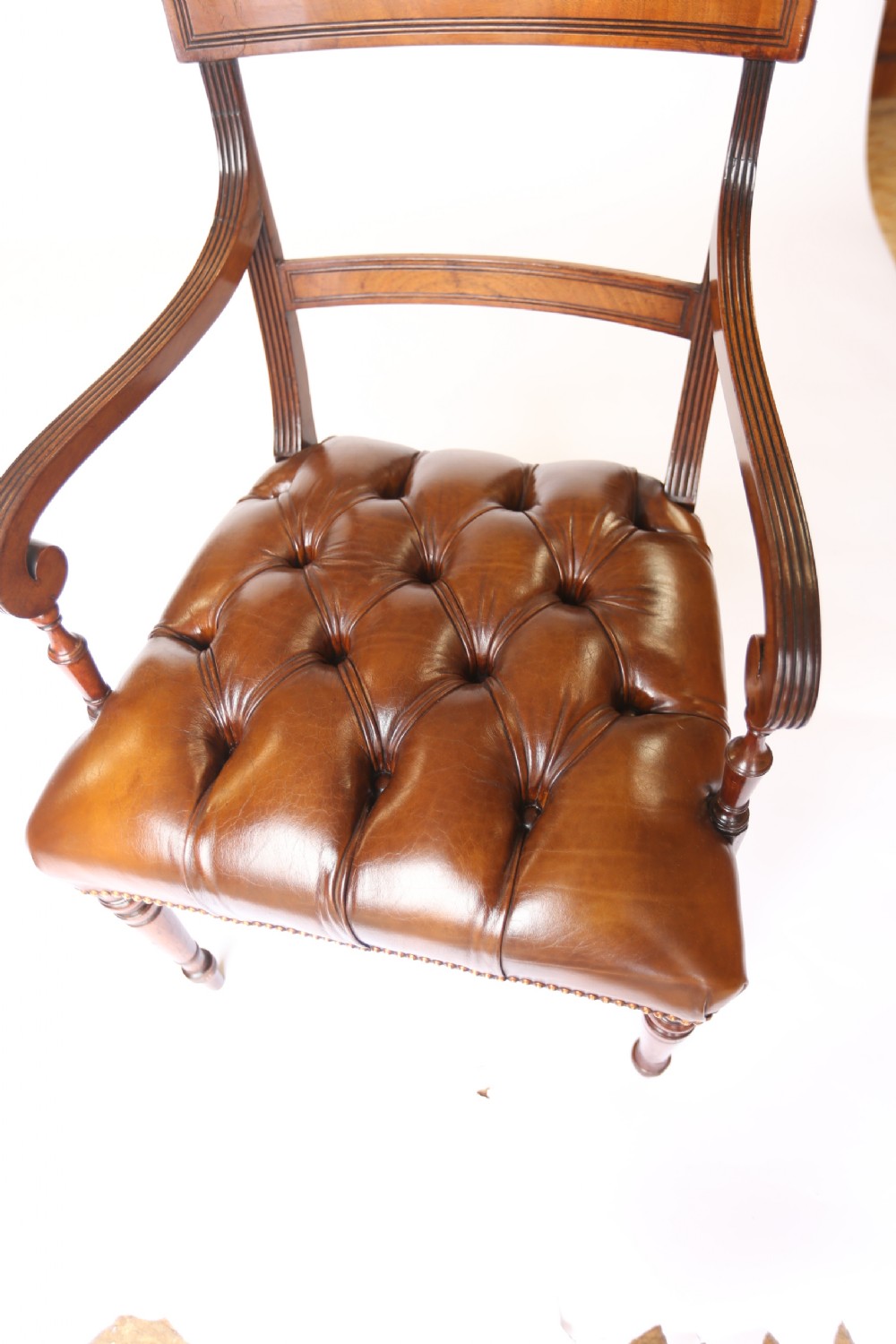 A pair of 19th-century mahogany elbow chairs featuring reeded arms, button-tufted brown leather seats with brass studding, and turned front legs. View VII