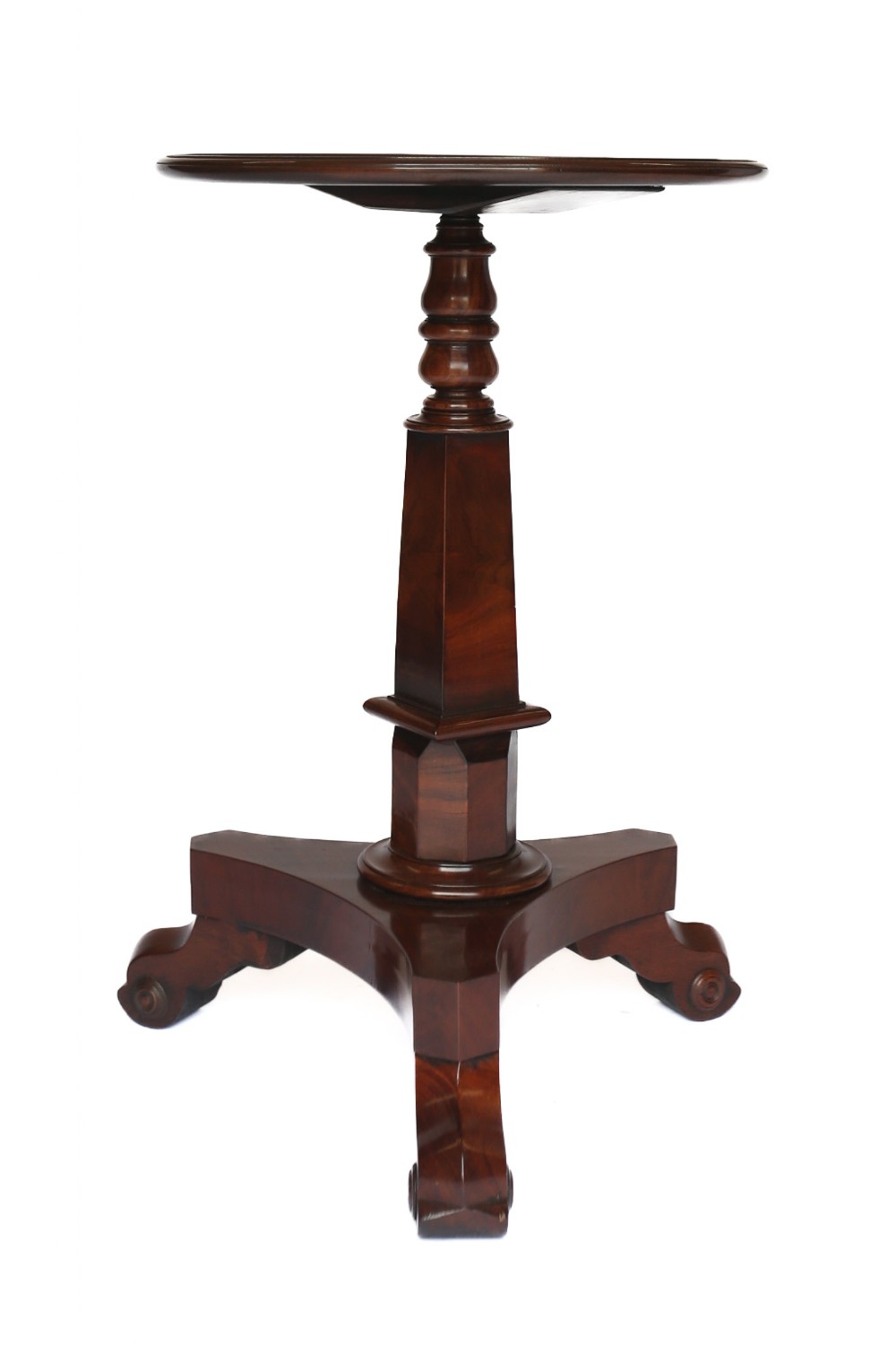 An antique mahogany lamp table featuring a round top supported by a turned pedestal stem and a triform base on scroll feet.