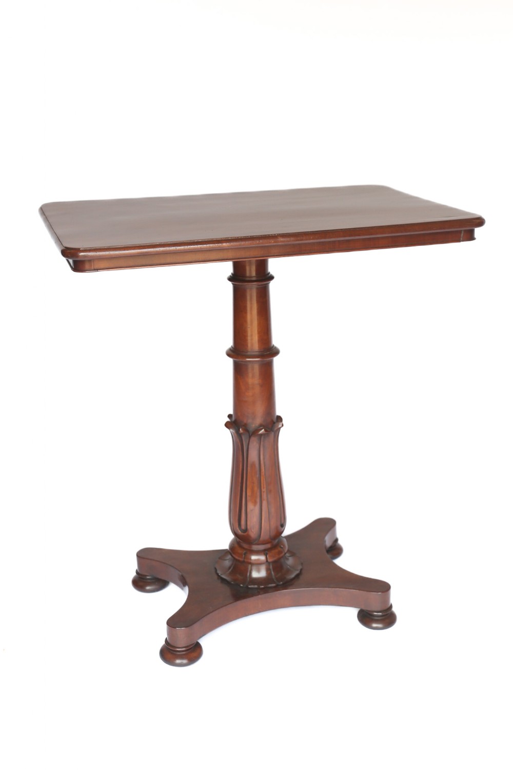 An antique William IV mahogany lamp table featuring a rectangular top, a turned and carved central pedestal stem, and a concave quadform plinth base resting on flattened disc feet.