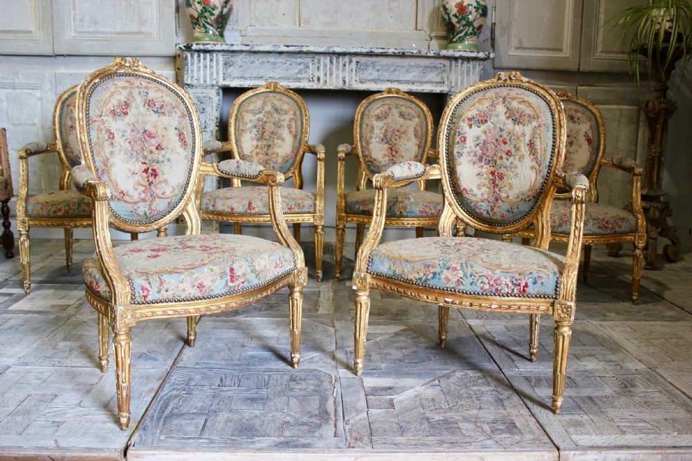 A set of six 18th-century Louis XVI French giltwood armchairs featuring oval medallion backs, carved armrests, fluted legs, and floral tapestry upholstery. View II