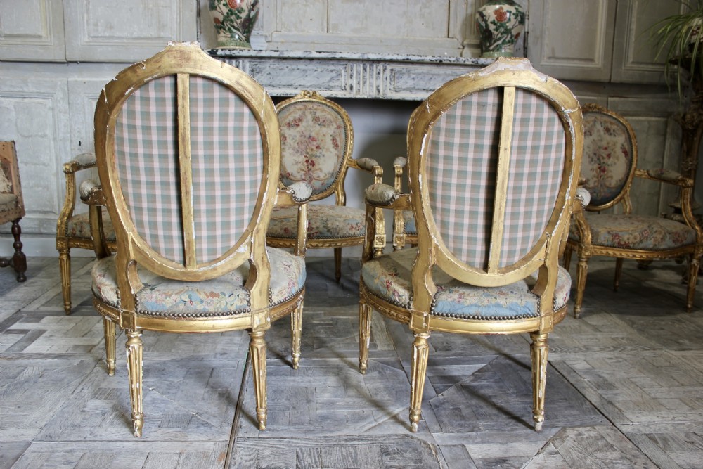 A set of six 18th-century Louis XVI French giltwood armchairs featuring oval medallion backs, carved armrests, fluted legs, and floral tapestry upholstery. View IV