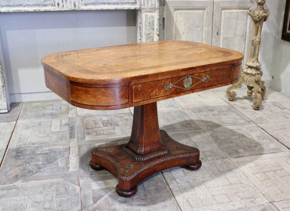 A Regency period pollard oak centre table featuring a rounded rectangular top with drawers, resting on a central pedestal and a shaped quadform base.