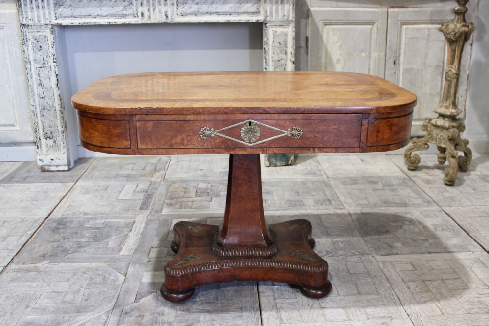 A Regency period pollard oak centre table featuring a rounded rectangular top with drawers, resting on a central pedestal and a shaped quadform base. View II
