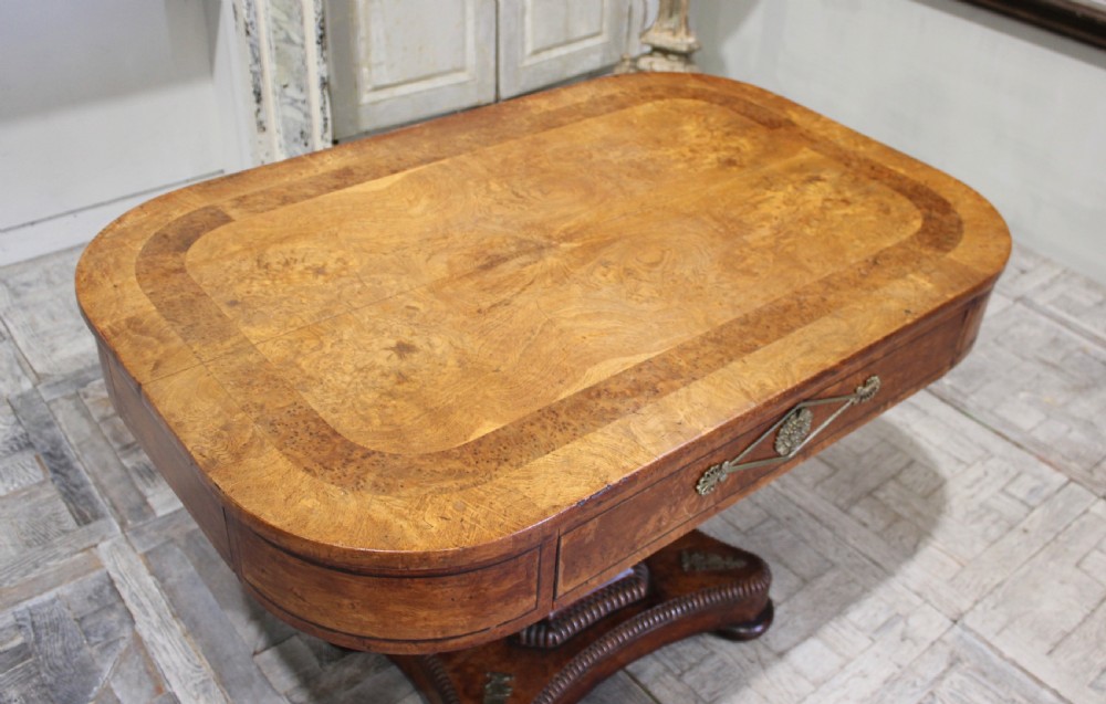 A Regency period pollard oak centre table featuring a rounded rectangular top with drawers, resting on a central pedestal and a shaped quadform base. View V
