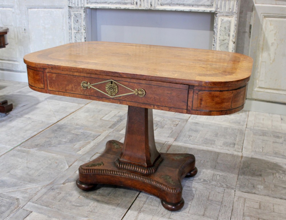 A Regency period pollard oak centre table featuring a rounded rectangular top with drawers, resting on a central pedestal and a shaped quadform base. View VI