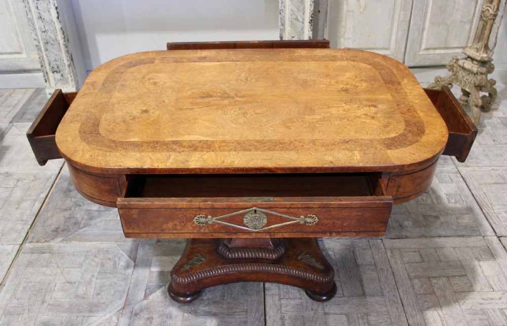 A Regency period pollard oak centre table featuring a rounded rectangular top with drawers, resting on a central pedestal and a shaped quadform base. View VIII
