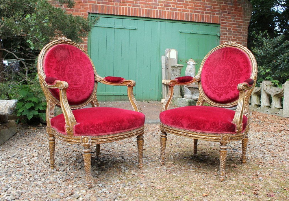 A pair of 19th-century French Louis XVI style giltwood armchairs upholstered in patterned red damask velvet with carved medallion backrests.