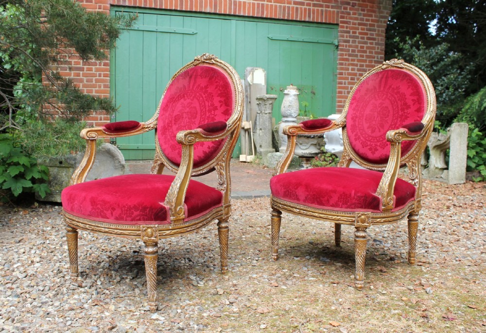 A pair of 19th-century French Louis XVI style giltwood armchairs upholstered in patterned red damask velvet with carved medallion backrests. View II