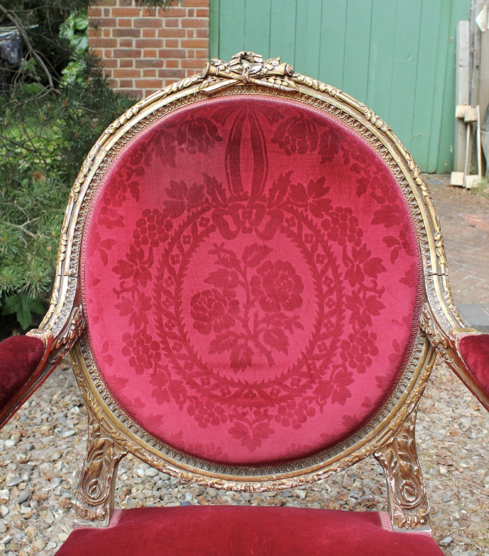 A pair of 19th-century French Louis XVI style giltwood armchairs upholstered in patterned red damask velvet with carved medallion backrests. View V