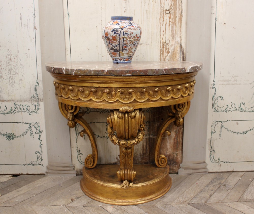 An 18th-century demilune console table featuring a carved giltwood frame with wave frieze detailing and a variegated marble top.