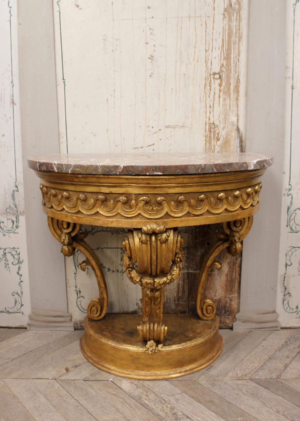 An 18th-century demilune console table featuring a carved giltwood frame with wave frieze detailing and a variegated marble top. View II