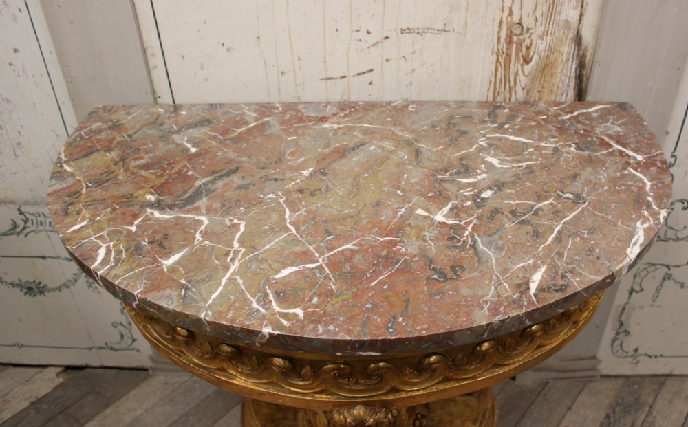 An 18th-century demilune console table featuring a carved giltwood frame with wave frieze detailing and a variegated marble top. View V