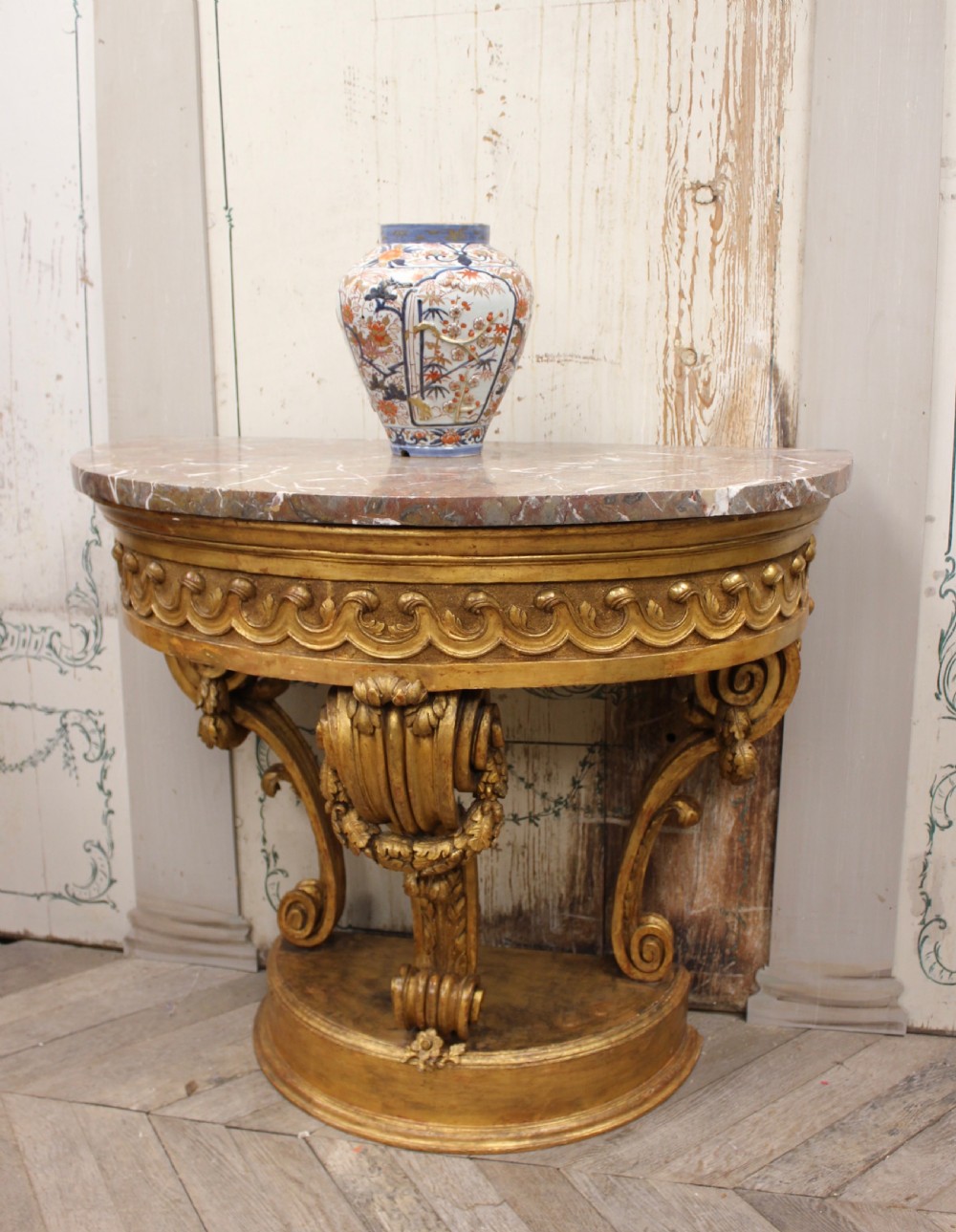 An 18th-century demilune console table featuring a carved giltwood frame with wave frieze detailing and a variegated marble top. View VI