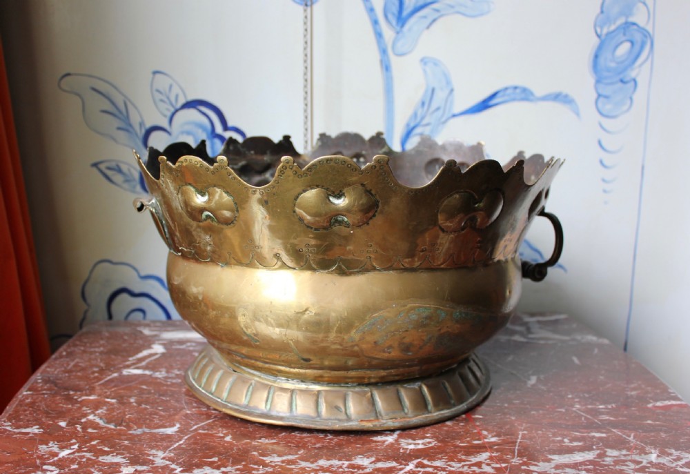 An 18th-century brass monteith bowl featuring a scalloped rim, embossed strapwork motifs, two side loop handles, and a gadrooned foot.