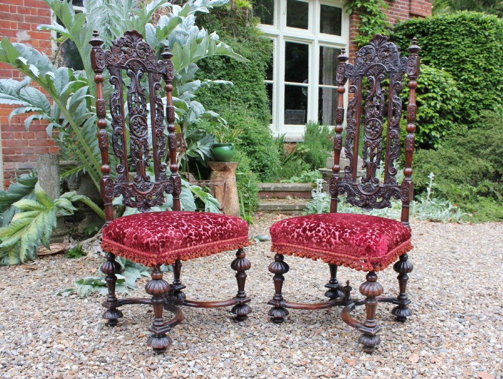 A pair of late 17th-century Baroque side chairs crafted from carved dark walnut with tall pierced backs, red velvet upholstered seats with fringed trim, and turned legs.