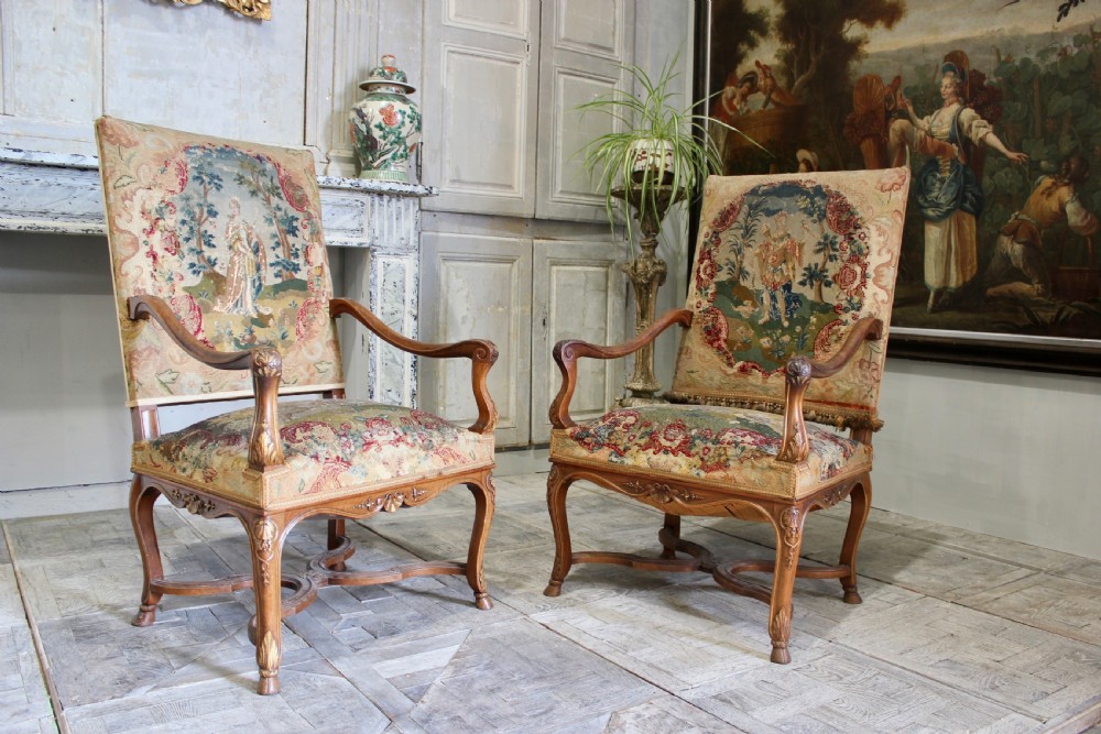 A pair of 19th-century French wooden armchairs with carved floral frames, curved armrests, and high backrests upholstered in woven figural tapestry.