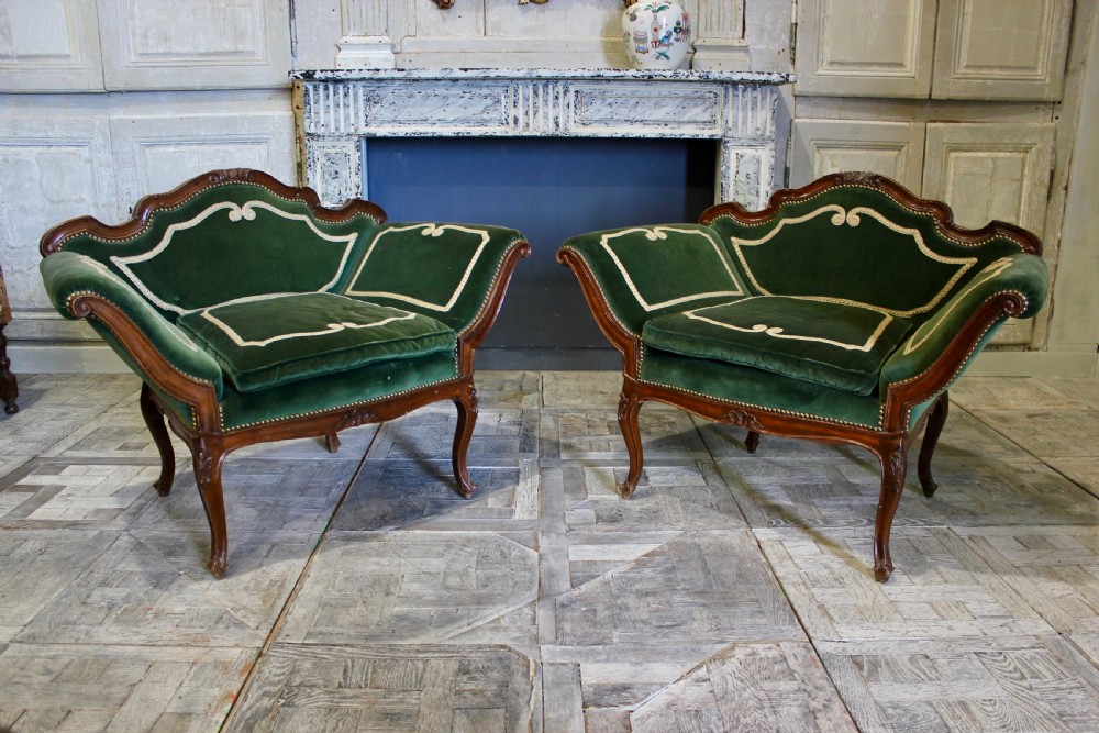 A pair of mid-19th century French Rococo revival armchairs upholstered in forest green velvet with contrasting cream braided trim and carved timber frames.