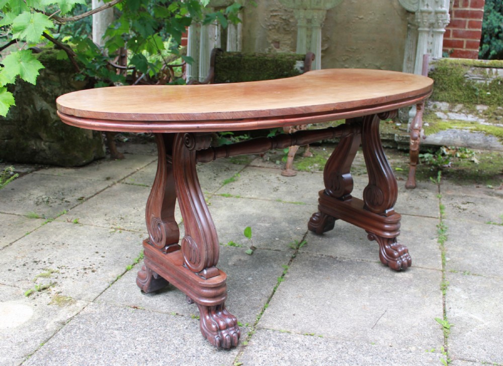 An early 19th-century mahogany kidney-shaped writing table with carved scroll trestle legs, a turned stretcher, and carved claw feet.
