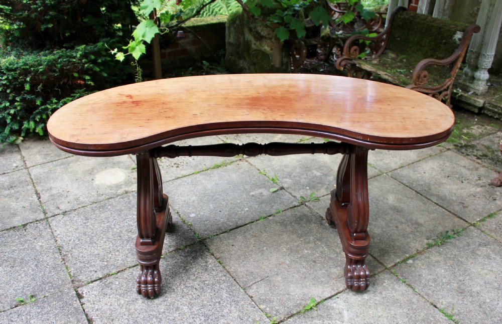 An early 19th-century mahogany kidney-shaped writing table with carved scroll trestle legs, a turned stretcher, and carved claw feet. View IX