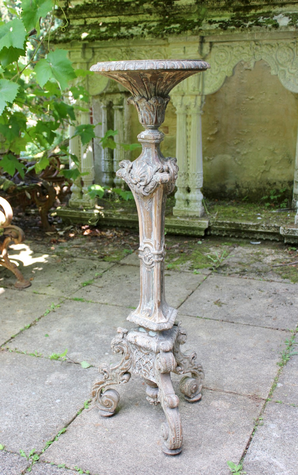 A tall, 19th-century carved wood torchere featuring a distressed weathered grey finish, detailed acanthus leaf carvings, and a tripod scroll base.