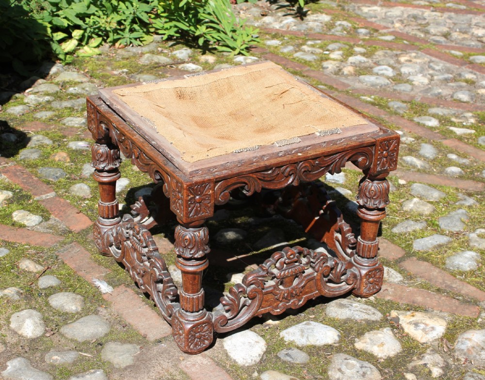 A square dark wood Batavian Baroque stool featuring carved floral aprons, turned baluster legs, pierced stretchers, and a hessian upholstered top. View II