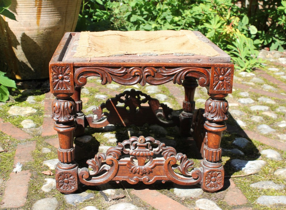 A square dark wood Batavian Baroque stool featuring carved floral aprons, turned baluster legs, pierced stretchers, and a hessian upholstered top. View IV