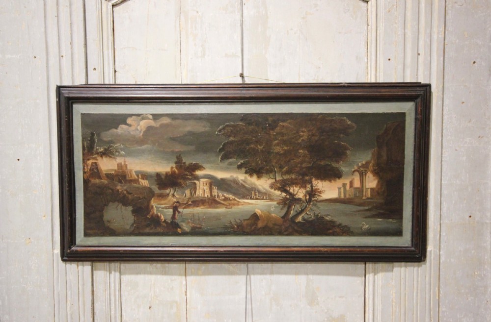 A horizontal 18th-century oil painting on a timber panel depicting a classical landscape with architectural ruins, river, trees, and dark moulded frame.