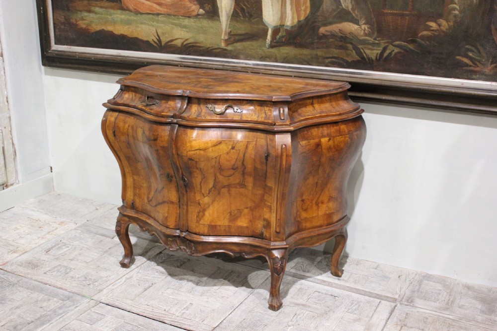 A 19th-century walnut bombe commode featuring serpentine front doors, two upper drawers with brass handles, and carved cabriole legs.