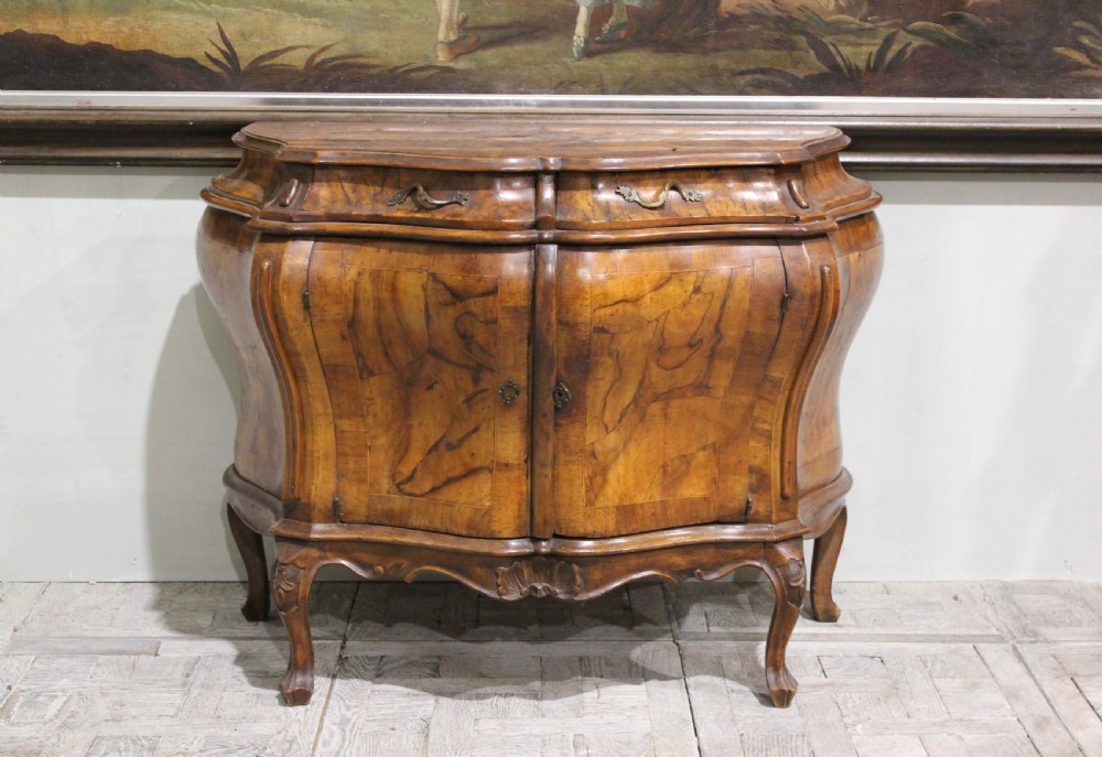 A 19th-century walnut bombe commode featuring serpentine front doors, two upper drawers with brass handles, and carved cabriole legs. View II
