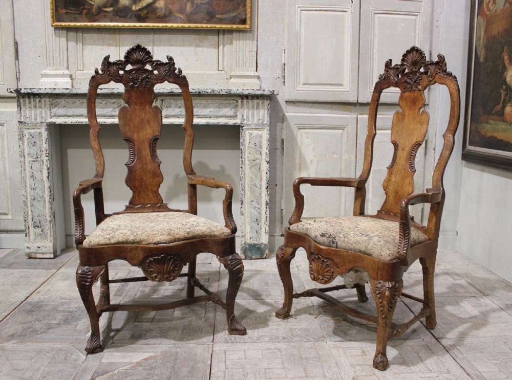 A pair of 18th-century carved walnut armchairs featuring tall backs with shaped splats, carved shell cresting, cabriole legs, and pattern upholstered drop-in seats.