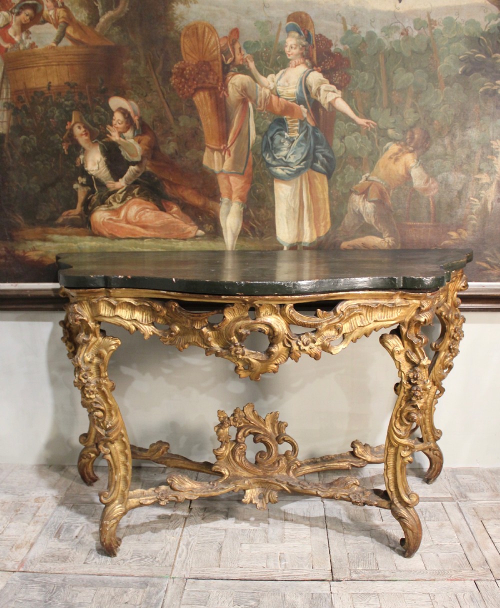 An 18th-century Italian Rococo carved giltwood console table featuring a dark serpentine top, openwork apron, scrolled cabriole legs, and a carved central stretcher.