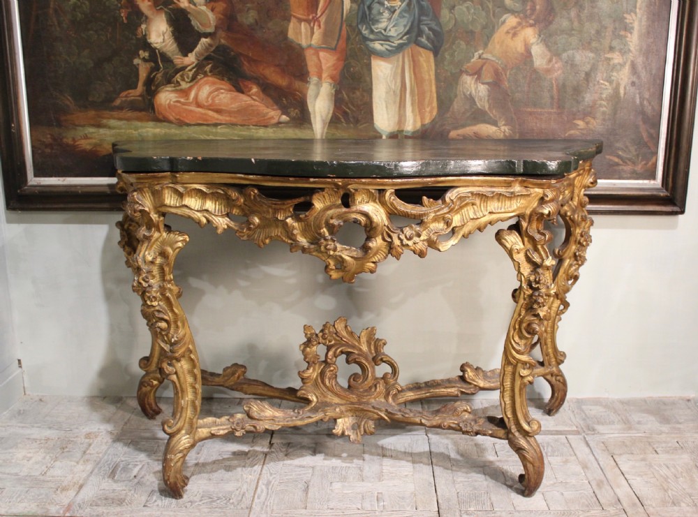 An 18th-century Italian Rococo carved giltwood console table featuring a dark serpentine top, openwork apron, scrolled cabriole legs, and a carved central stretcher. View II