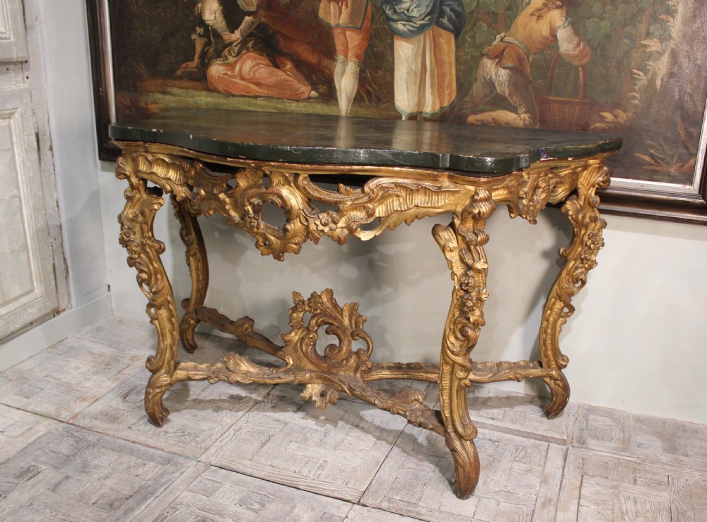 An 18th-century Italian Rococo carved giltwood console table featuring a dark serpentine top, openwork apron, scrolled cabriole legs, and a carved central stretcher. View III