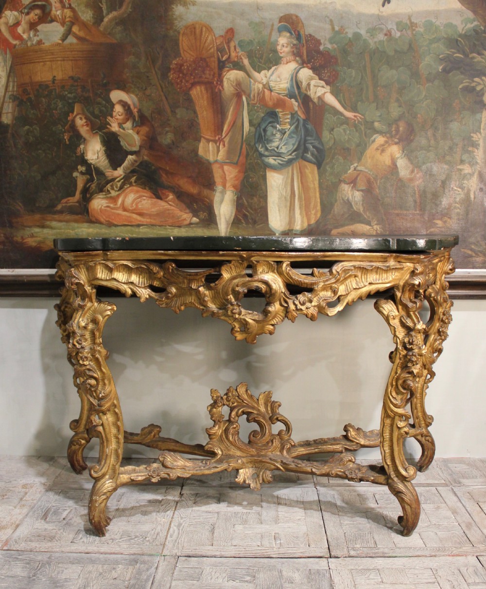 An 18th-century Italian Rococo carved giltwood console table featuring a dark serpentine top, openwork apron, scrolled cabriole legs, and a carved central stretcher. View IV