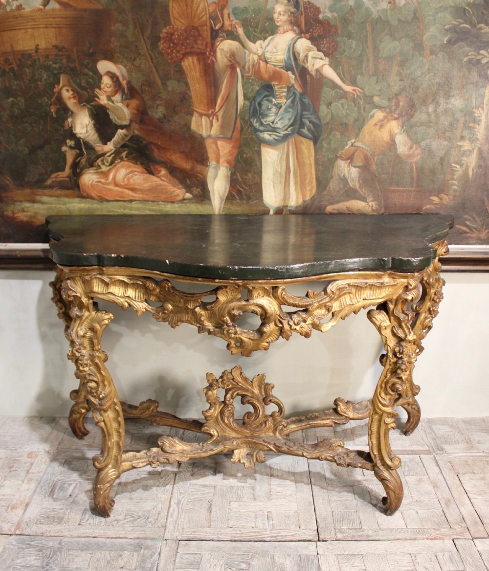 An 18th-century Italian Rococo carved giltwood console table featuring a dark serpentine top, openwork apron, scrolled cabriole legs, and a carved central stretcher. View VI