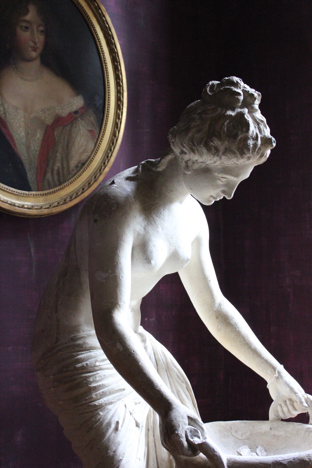 A full-length off-white plaster statue depicting a classical draped female figure standing beside a pedestal basin. View II
