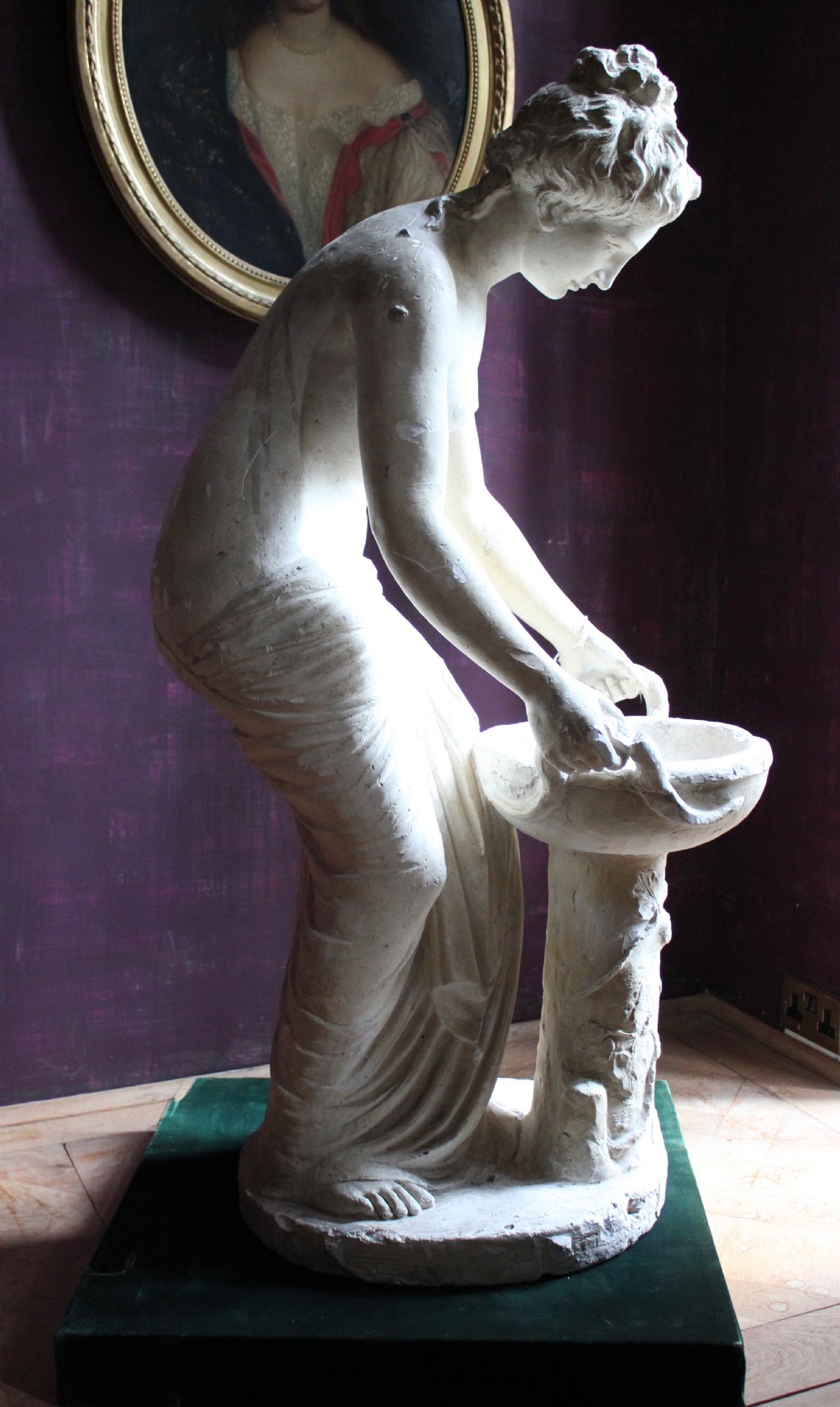 A full-length off-white plaster statue depicting a classical draped female figure standing beside a pedestal basin. View IV