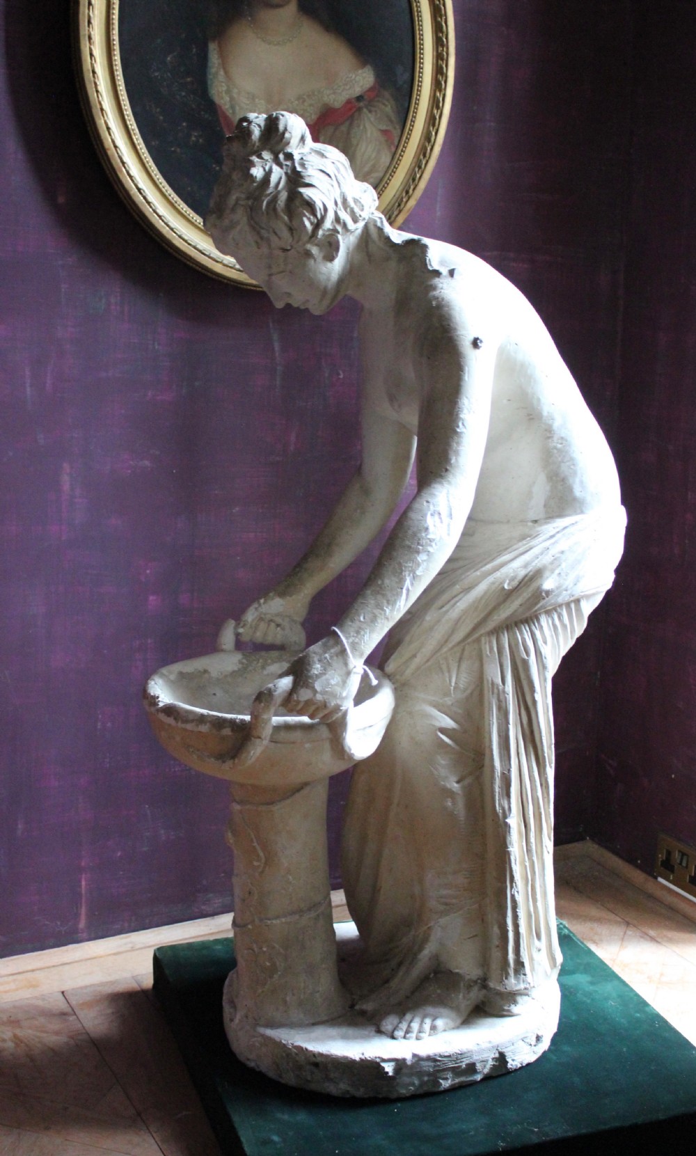A full-length off-white plaster statue depicting a classical draped female figure standing beside a pedestal basin. View VI
