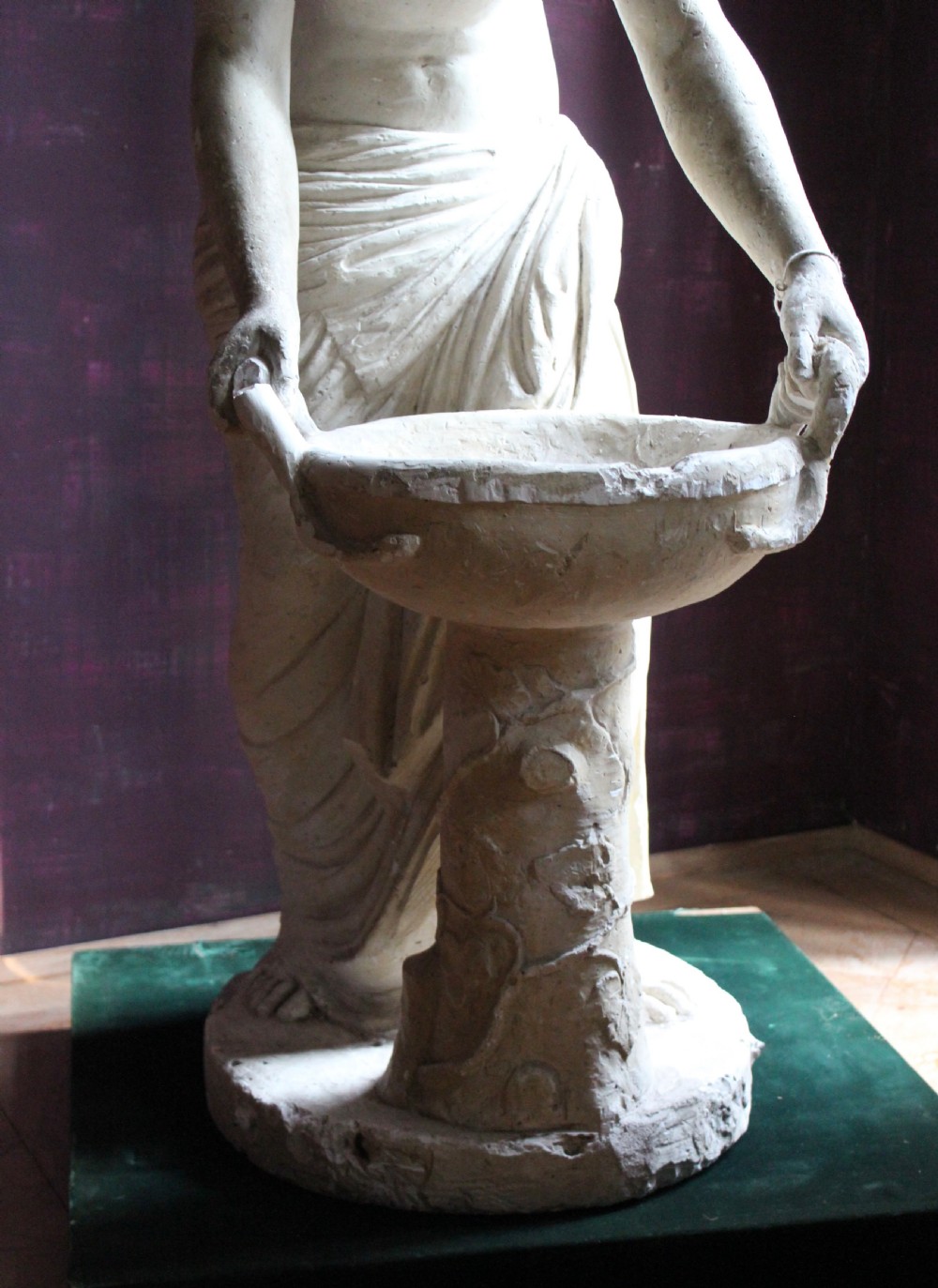 A full-length off-white plaster statue depicting a classical draped female figure standing beside a pedestal basin. View VII