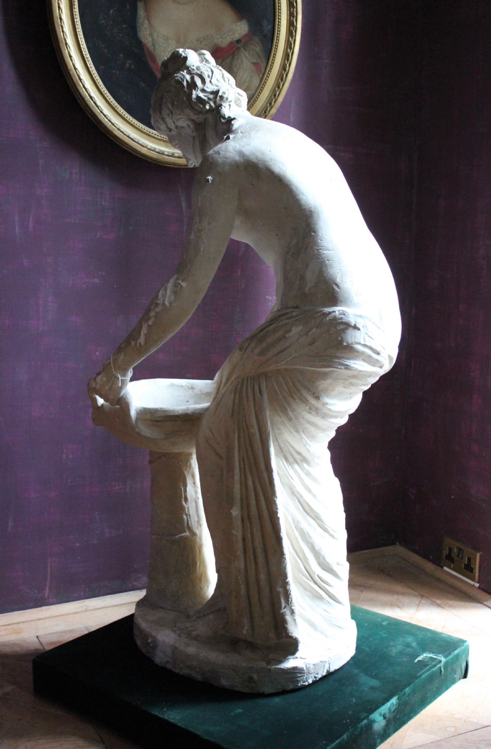 A full-length off-white plaster statue depicting a classical draped female figure standing beside a pedestal basin. View VIII