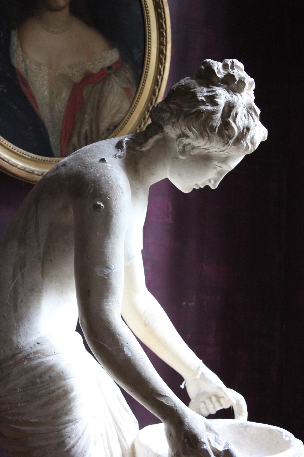 A full-length off-white plaster statue depicting a classical draped female figure standing beside a pedestal basin. View XI